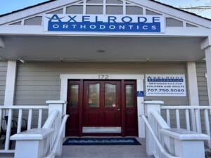 Front entrance of Axelrode Orthodontics, featuring a red door, accessibility signage, and business branding with contact details.
