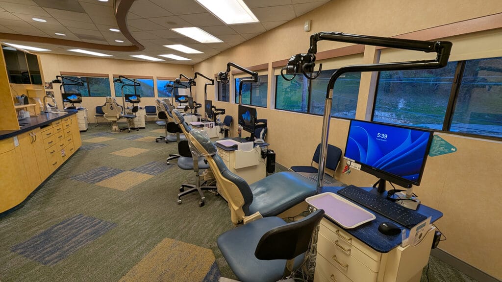 A modern orthodontic treatment room at Axelrode Orthodontics, featuring multiple dental chairs, computer workstations, and overhead dental equipment in a comfortable setting.