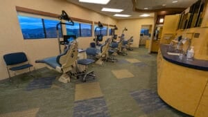 A modern orthodontic clinic with multiple dental chairs, overhead screens, and large windows overlooking a scenic landscape.